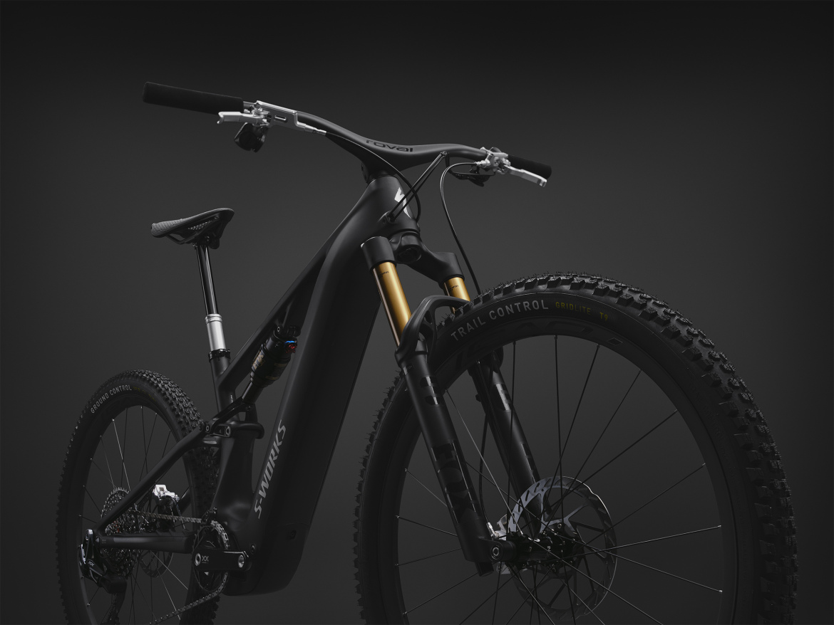 A sleek, modern electric mountain bike featuring a black frame with a matte finish, gold suspension components, and rugged tires. The image focuses on the bike's front half, highlighting its advanced design and technical features against a dark background. The handlebars are visible, showing a clean setup with minimalistic controls.