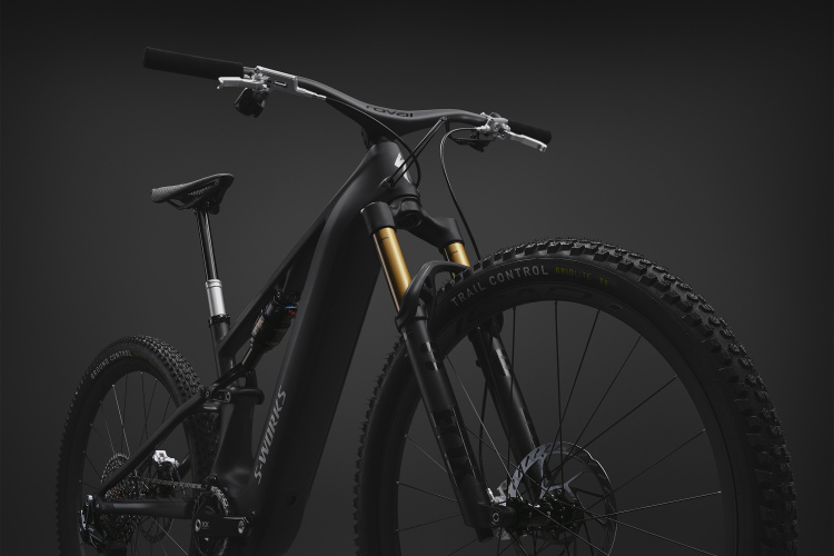 A sleek, modern electric mountain bike featuring a black frame with a matte finish, gold suspension components, and rugged tires. The image focuses on the bike's front half, highlighting its advanced design and technical features against a dark background. The handlebars are visible, showing a clean setup with minimalistic controls.