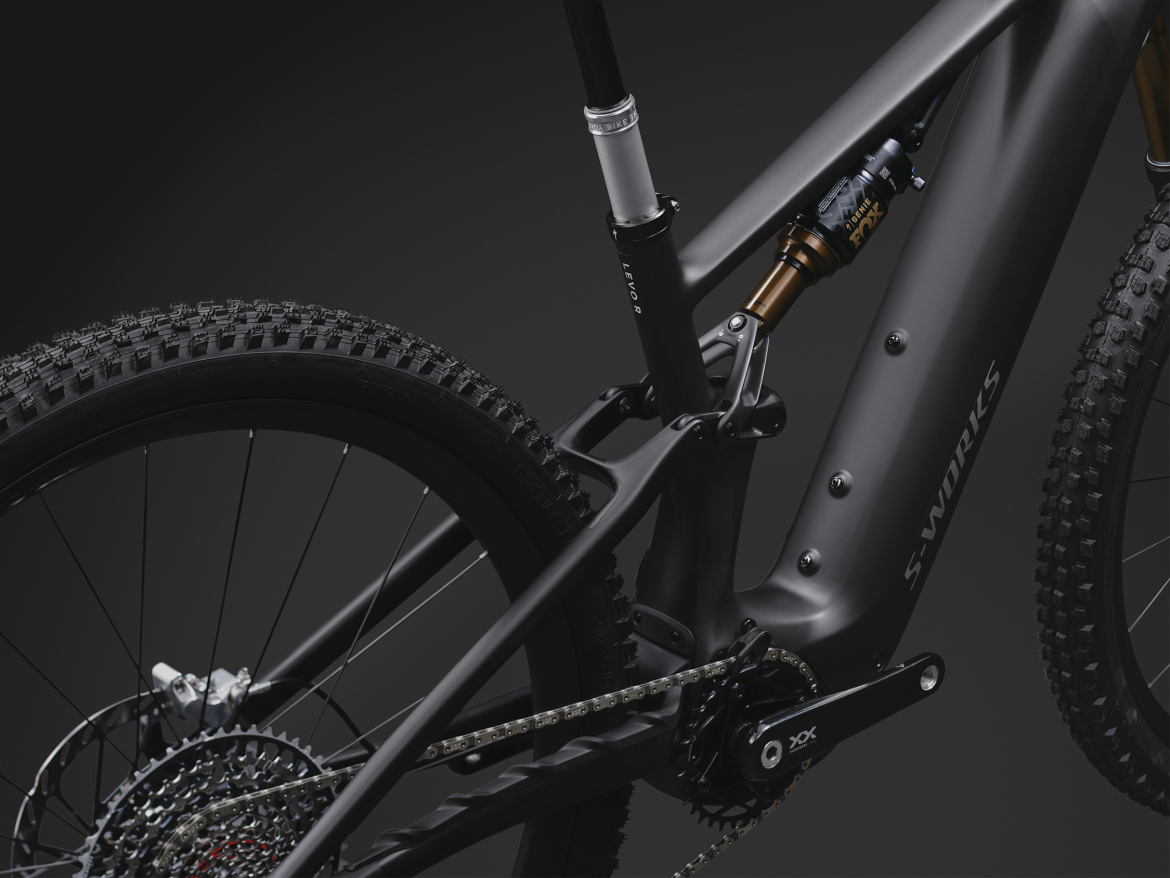 Close-up view of the rear section of a mountain bike showcasing the sleek design and advanced components, including the suspension, drivetrain, and tire tread on a dark background. The bike features a matte finish with prominent branding on the frame.