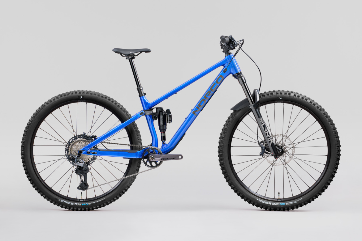 A blue mountain bike with a lightweight frame, showcasing a suspension system, wide tires, and a modern design. The bike is positioned against a light gray background, highlighting its features such as disc brakes and a geared drivetrain.