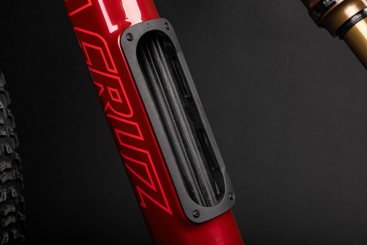 Close-up of a red bicycle frame showcasing a sleek black protective guard over a vent, designed for durability and performance. The frame features bold graphics and is set against a dark background.