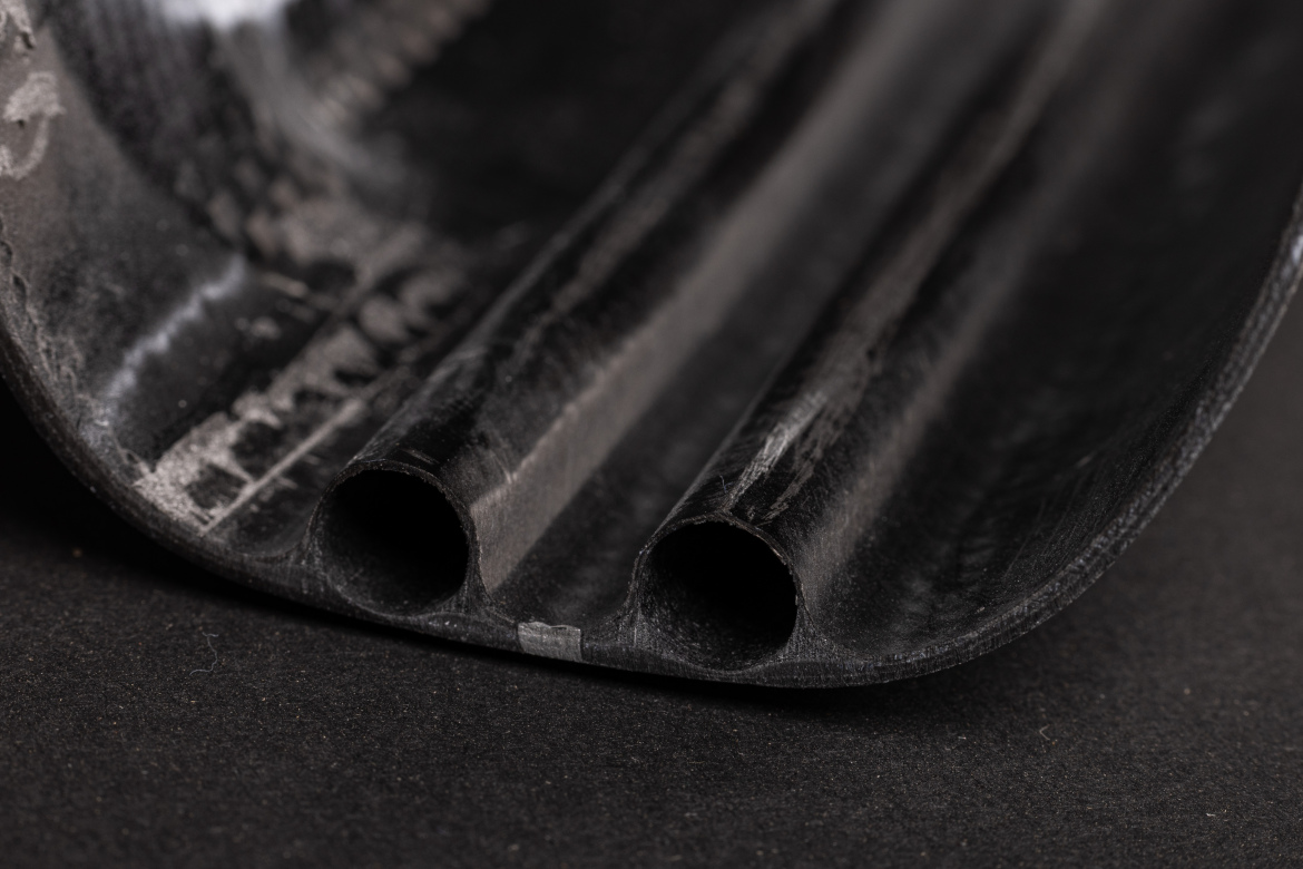 Close-up view of a black, textured object with two hollow tubes, set against a dark background. The surface features subtle markings and a smooth curve at the edges, suggesting a flexible material.