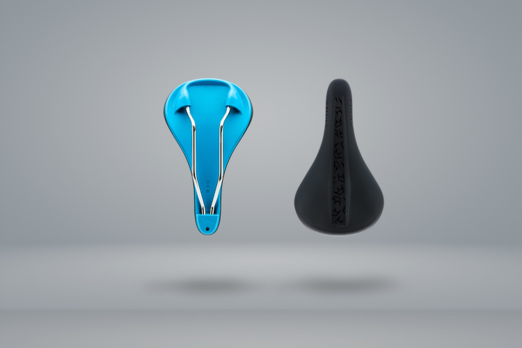 Two bicycle saddles are displayed side by side, one in a bright blue color with a sleek, minimalist design and the other in a matte black with a textured surface, both set against a light gray background.