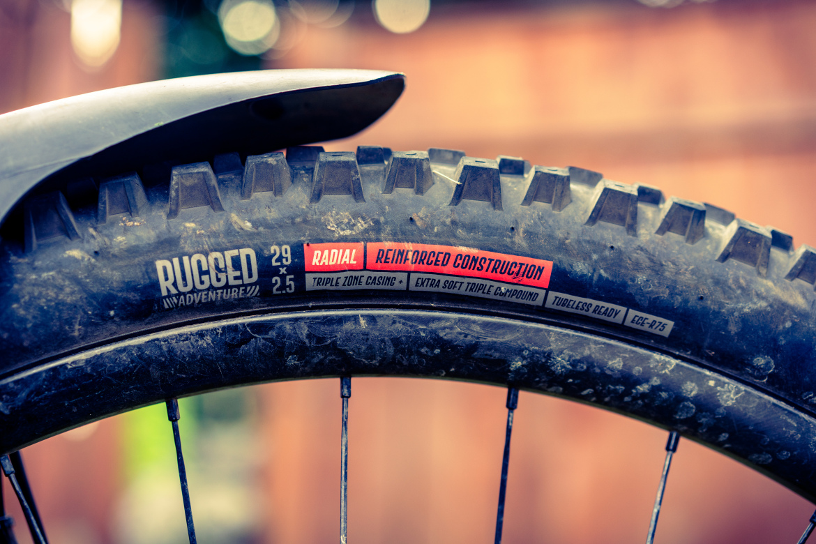 Close-up of a rugged mountain bike tire showing details such as "29 x 2.5," "Radial," "Reinforced Construction," and other specifications, with a blurred background.