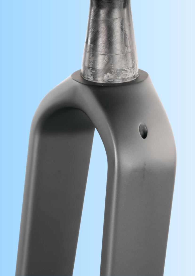 Close-up image of a bicycle fork made of metal with a smooth, matte black finish and a polished silver steerer tube. The background features a gradient of light blue shades.