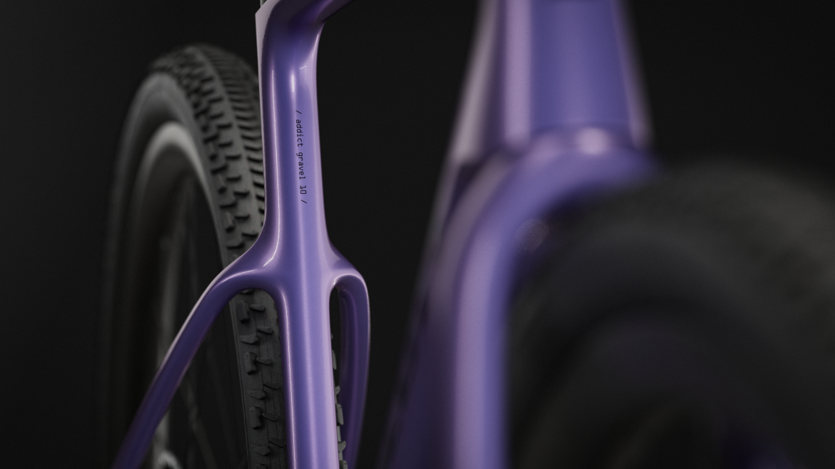 Close-up of a purple bicycle frame, showcasing the rear triangle and tire. The frame has a modern design with a smooth finish, and features text that reads “addict gravel 10” on the side. The background is black, enhancing the vibrant color of the bike.