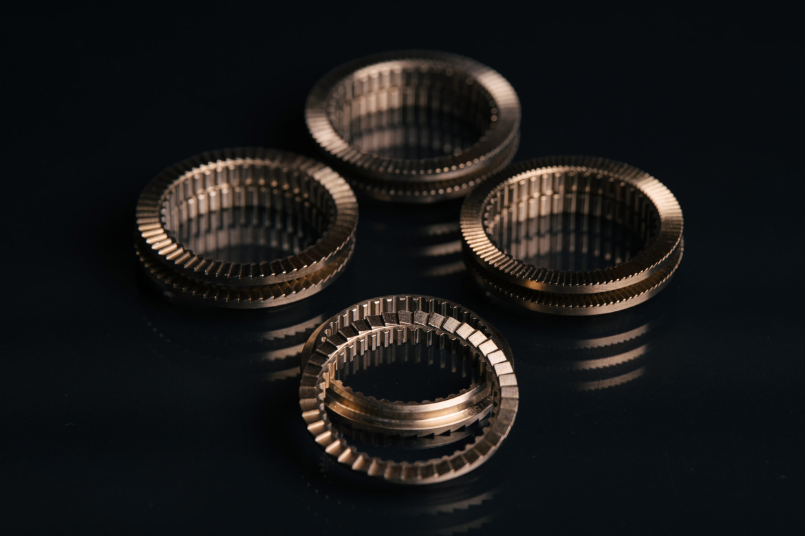 Four metallic rings with a ridged texture are arranged on a dark surface, reflecting light and casting subtle shadows. The rings vary in size and are positioned in a way that highlights their intricate designs.