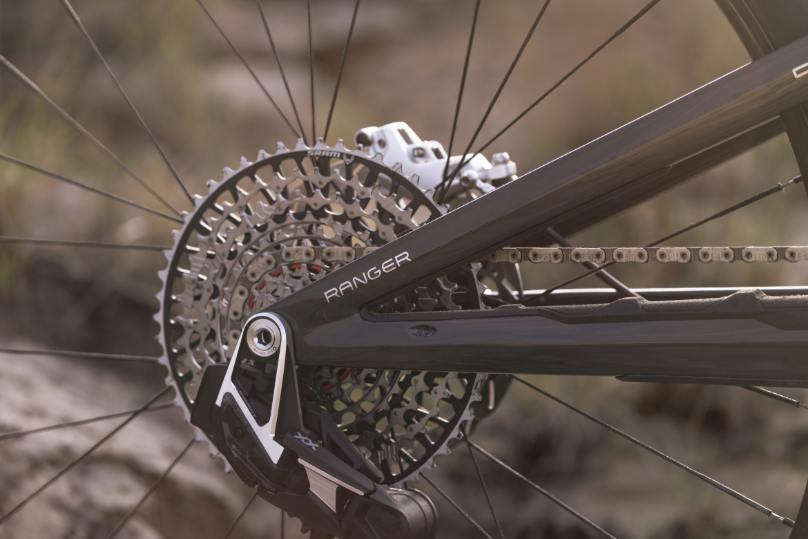 Close-up view of a bicycle's rear cassette and derailleur, showcasing the gear system and chain, with a focus on the details of the bike frame labeled "Ranger." The background features a natural outdoor setting with soft lighting.
