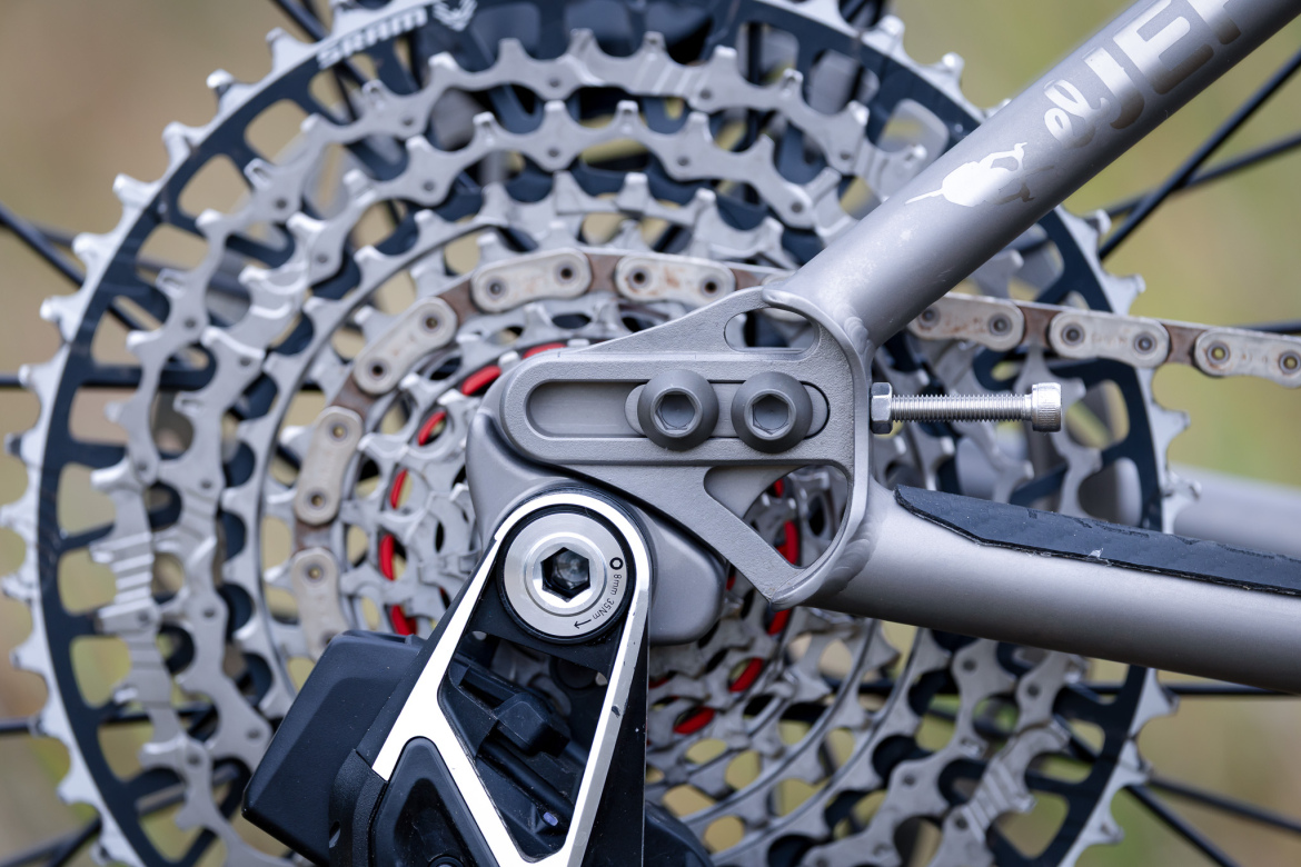 Close-up image of a bicycle's rear drivetrain, featuring the cassette and derailleur system. The intricate metallic details of the gears and chain links are clearly visible, showcasing the engineering involved in modern bike mechanics. The background is softly blurred, focusing attention on the components.