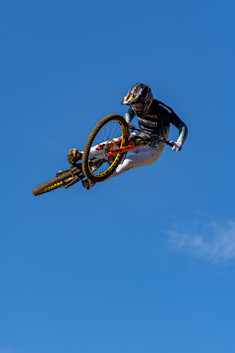 A mountain biker performing a mid-air trick against a clear blue sky, showcasing dynamic movement and skill while riding a yellow and black bike.