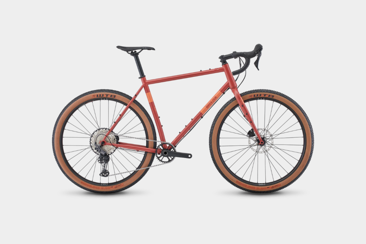 A red gravel bike with tan tires, featuring a lightweight frame, drop handlebars, and a multi-gear drivetrain, positioned against a white background.