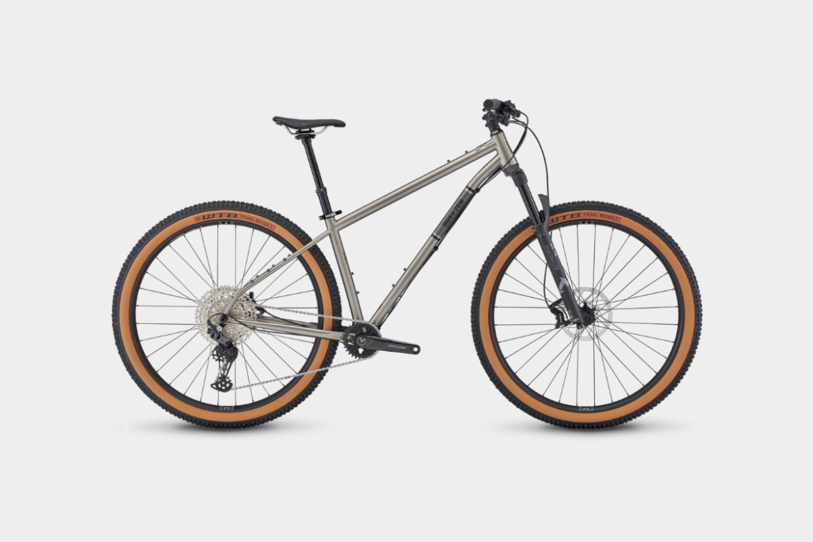A modern mountain bike with a sleek silver frame, featuring wide tires with brown rubber accents. The bike has a front suspension fork, a detailed drivetrain, and a comfortable saddle, positioned on a white background.