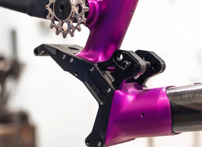 Close-up view of a purple bicycle frame featuring a sprocket and black components, highlighting the intricate design and engineering of the bike's structure.
