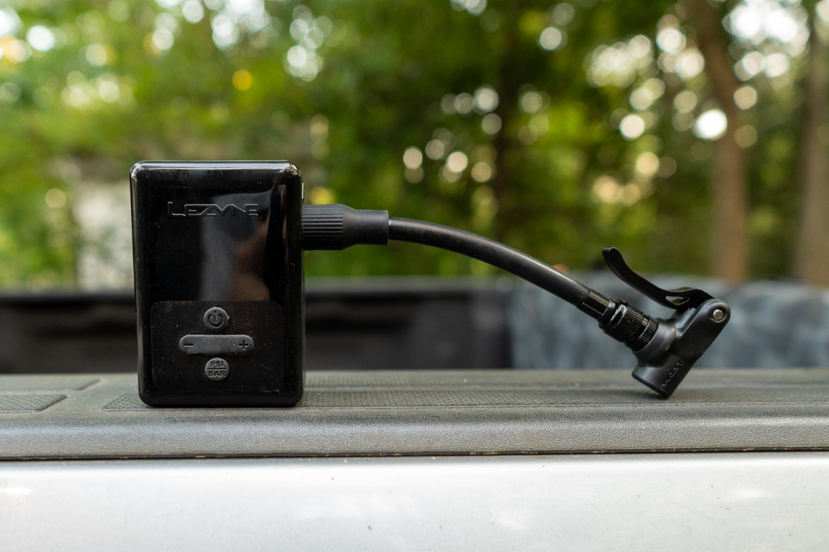 A Lezyne electronic tire pump with a pressure gauge and adjustable settings, positioned on a truck bed with a blurred natural background.
