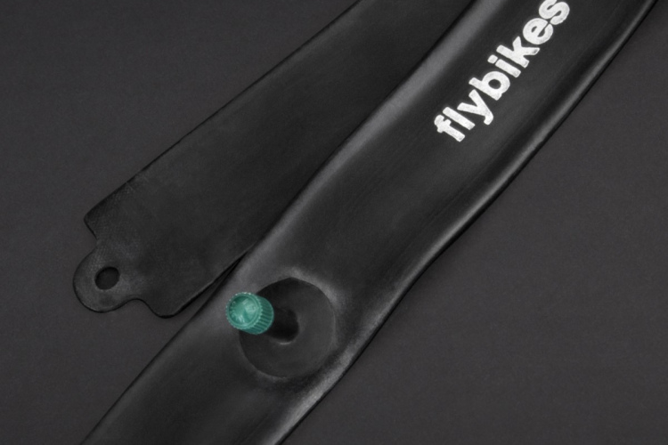 Close-up view of a black BMX tube with a green valve stem, featuring the text "flybikes cobra tube" printed in white. The tube is displayed against a dark background.