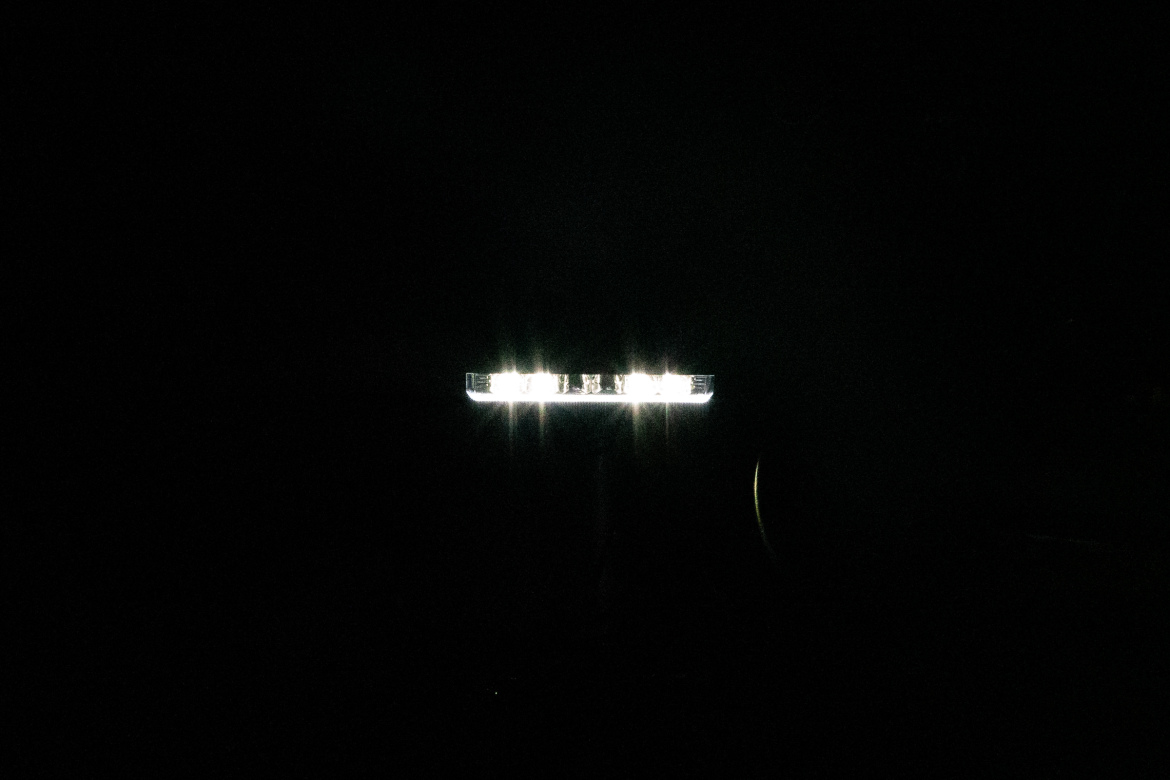 A bright light shining in a dark environment, partially illuminated text or symbols can be seen on the light source, with a mostly black background.